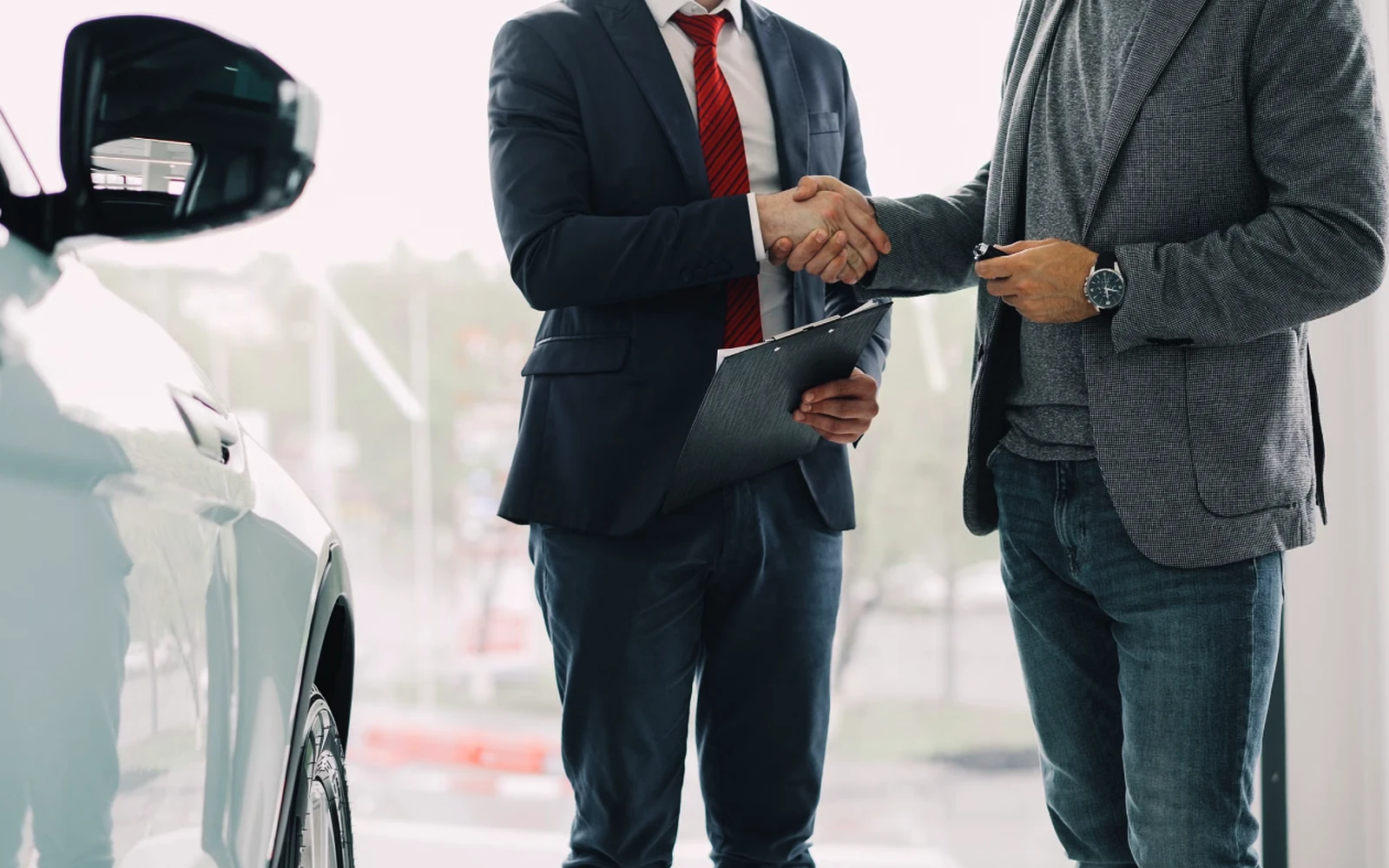 Agente de seguros dándole la mano a un cliente junto a su auto
